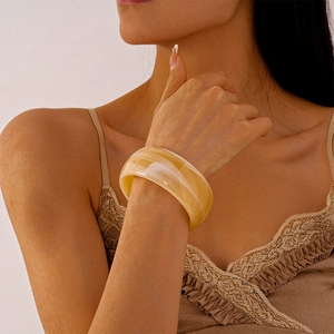 Detail of a wide amber resin bangle with marble texture worn by a model in soft light