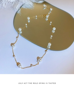 Close-up of elegant pearl necklace with gold chain displayed on a golden mirror