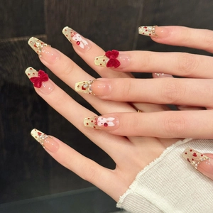Long trapezoid press-on nails with pink base, gold tips, and red velvet bows