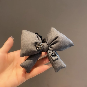 Detail of grey fabric bow hair tie with rhinestone center and silver camellia metal tag