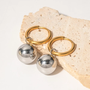 Detailed shot of two-tone 18K gold ring with a silver ball pendant on beige stone
