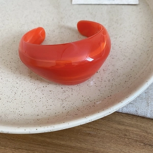 Detailed view of wide bright orange acrylic cuff bracelet on a minimalist ceramic plate