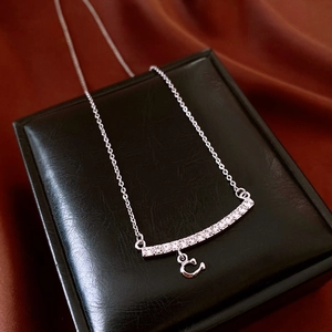 Macro shot of silver C-pendant necklace with pavé zircon stones on black leather