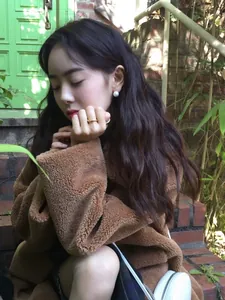 Detailed view of white pearl earrings paired with a brown teddy coat for autumn style