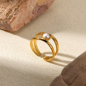 Detail of gold hammered open ring featuring a single white pearl on a textured stone base