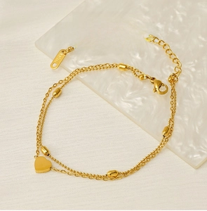 Detail of double-layer gold stainless steel anklet with heart pendant on water texture