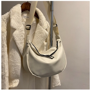 Detail of cream crescent crossbody bag featuring black zipper and wide nylon strap