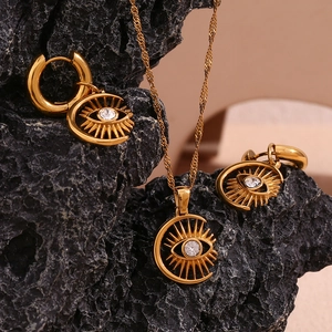 Detail of 18K gold evil eye pendant necklace and earrings set on black stone background