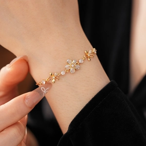 Détail d'un bracelet fleuri doré orné de zircons scintillants porté sur un poignet de femme