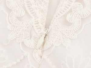 Dettaglio di elegante tessuto in pizzo bianco con ricami e chiusura a zip invisibile