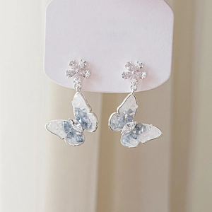 Détail de boucles d'oreilles papillon argentées avec dégradé bleu et clous floraux en cristal