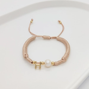 Detailed shot of handmade woven bracelet featuring a white pearl and golden letter H charm