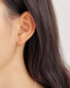 Close-up of minimalist gold cross hoop earrings with zircons worn on ear