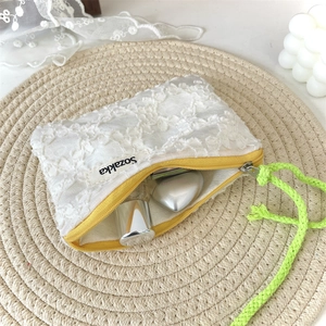 Détail de la pochette en dentelle florale blanche avec zip jaune et cordon tressé vert
