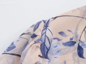 Détail du tissu en mousseline beige avec imprimés floraux bleus et épaule à volants chic