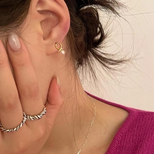 Macro detail of elegant gold knot pearl earrings and silver twisted ring worn by a model