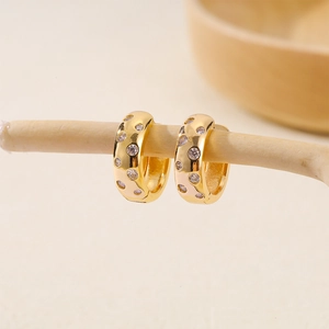 Macro detail of gold-plated hoop earrings with inlaid cubic zirconia on a wooden branch