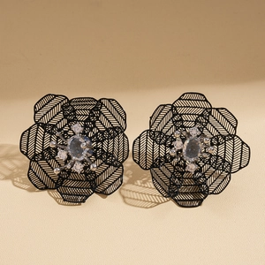 Macro shot of vintage hollow black floral earrings with blue drop-shaped center zircon stones