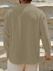 Detail view of the back of a men's loose linen shirt in khaki with a natural rock background