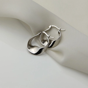 Detailed view of irregular silver wave earrings with S925 mark on white silk