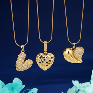 Three gold heart pendants with cubic zirconia on snake chains against blue background