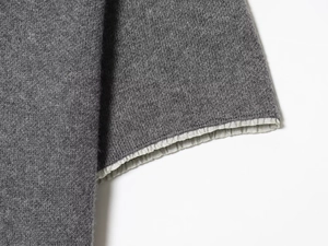 Detail of grey knitted dress sleeve featuring elegant white pleated ruffle cuff design