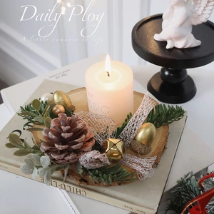 Close-up of a Christmas candle on wood base with pine cones and golden bells decoration