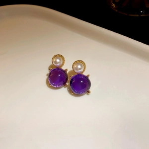 Close-up of vintage gold earrings with pearls and purple faceted gemstones on a tray