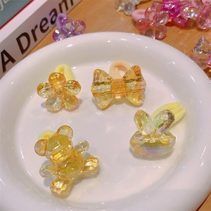 Detail of cute yellow resin hair ties featuring bear, rabbit, and flower shapes in a dish