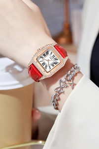 Close-up of a square rose gold watch with crystals and a red leather strap on a wrist