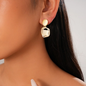 Gros plan d'une boucle d'oreille carrée dorée avec opale centrale et bordure en strass