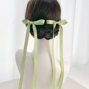 Detail of light green satin ribbon bow hair clips worn on back of a braided hairstyle