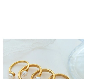 Macro detail of gold U-shaped open rings featuring elegant white pearls on a soft fabric