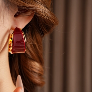 Close-up of a model wearing a gold hoop earring with deep red resin inlay detailing