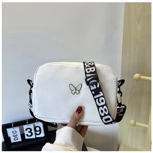 Detailed close-up of white nylon crossbody bag with metal butterfly and branded wide strap