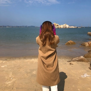 Detail view of purple rainbow knit gloves worn in a scenic seaside outdoor setting