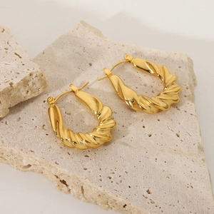 Detailed close-up of gold-plated twisted hoop earrings on a textured stone surface