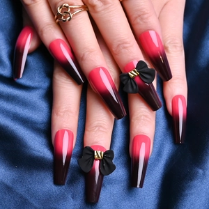 Detail of long T-shape press-on nails with red-black gradient and 3D black bow accents