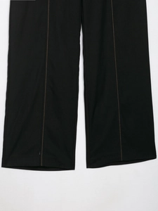 Detailed close-up of black wide-leg trousers featuring vertical golden contrast stitching