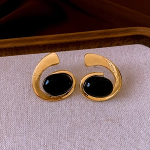 Detailed view of vintage gold earrings with black oval gemstone on linen fabric backdrop