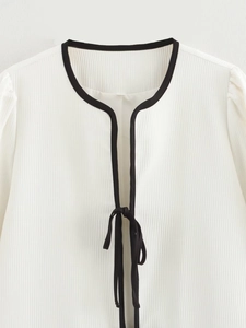 Detailed close-up of textured pleated fabric with black contrast trim on white cardigan
