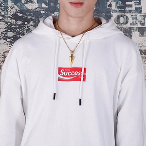 Macro detail of golden arrow pendant on a twisted chain worn with streetwear