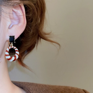 Detail of enamel geometric earrings with red and white stripes and gold accents on model