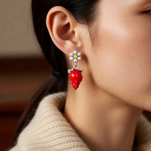 Close-up of red strawberry earrings with white pearl and daisy flower on a model
