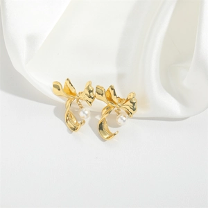 Elegant gold bow earrings with white pearl pendants displayed on white satin fabric