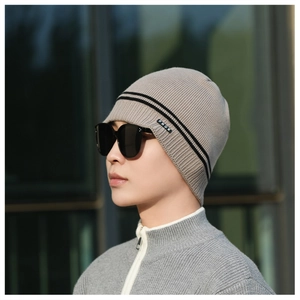 Close-up of grey knit beanie with black stripes and logo tag on outdoor model