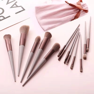 Flat lay of 13 professional makeup brushes with a pink velvet drawstring bow bag