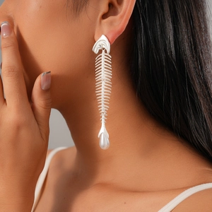 Close-up of a silver fishbone earring with a white pearl drop worn by a model