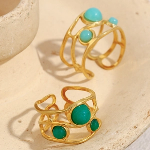 Detail of 18K gold-plated open rings with green and blue gemstones on a stone plate