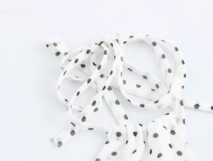 Détail d'une attache en tissu blanc à pois montrant la texture douce et la matière légère